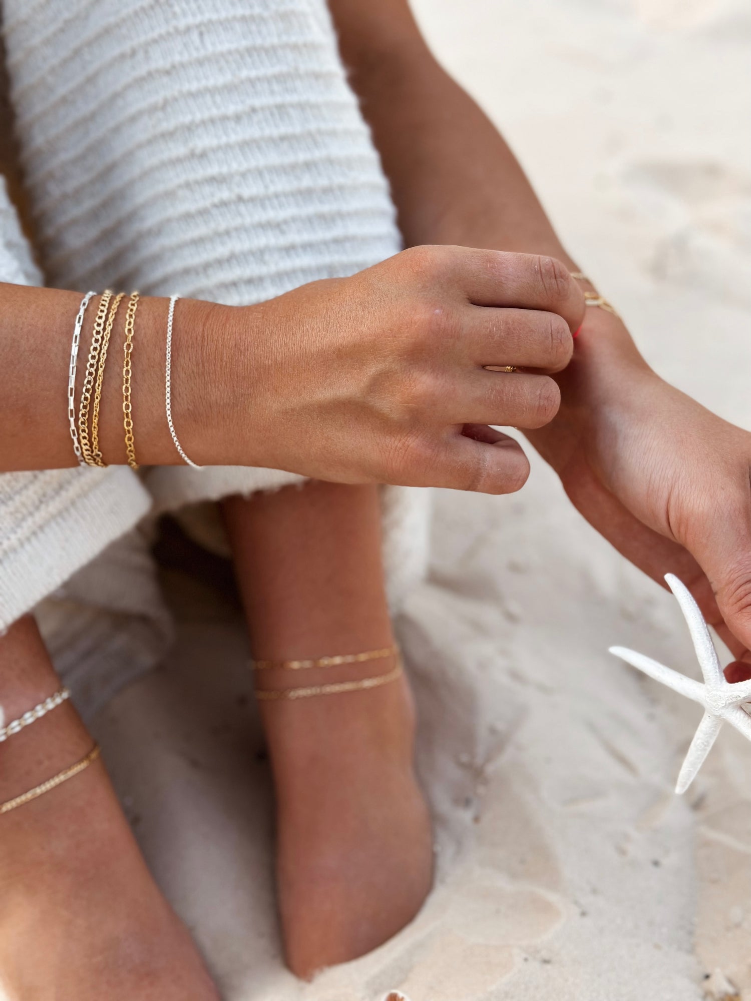 Woman on a beach wearing fused jewellery bracelets and ankle chains in gold and silver